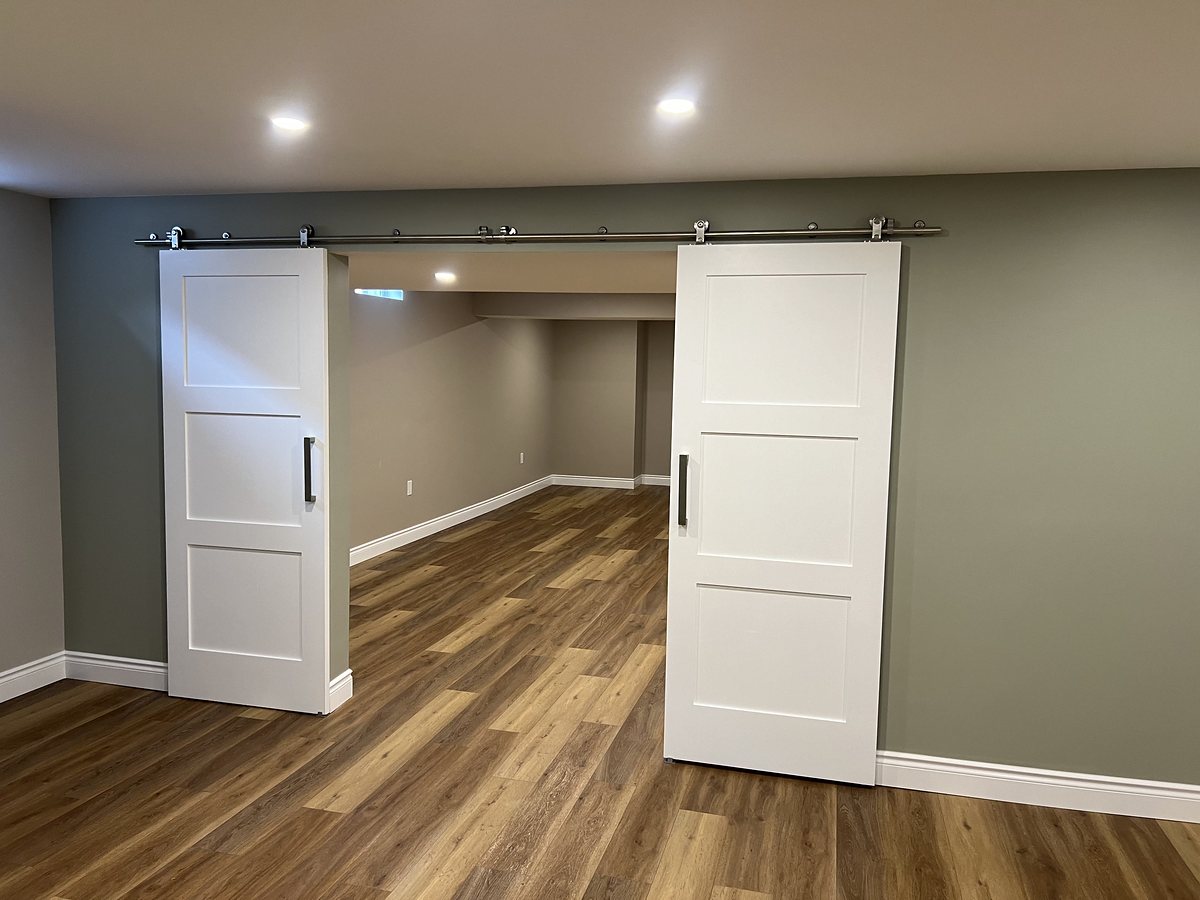 Finished basement with two white barn doors on a steel track against a sage accent wall