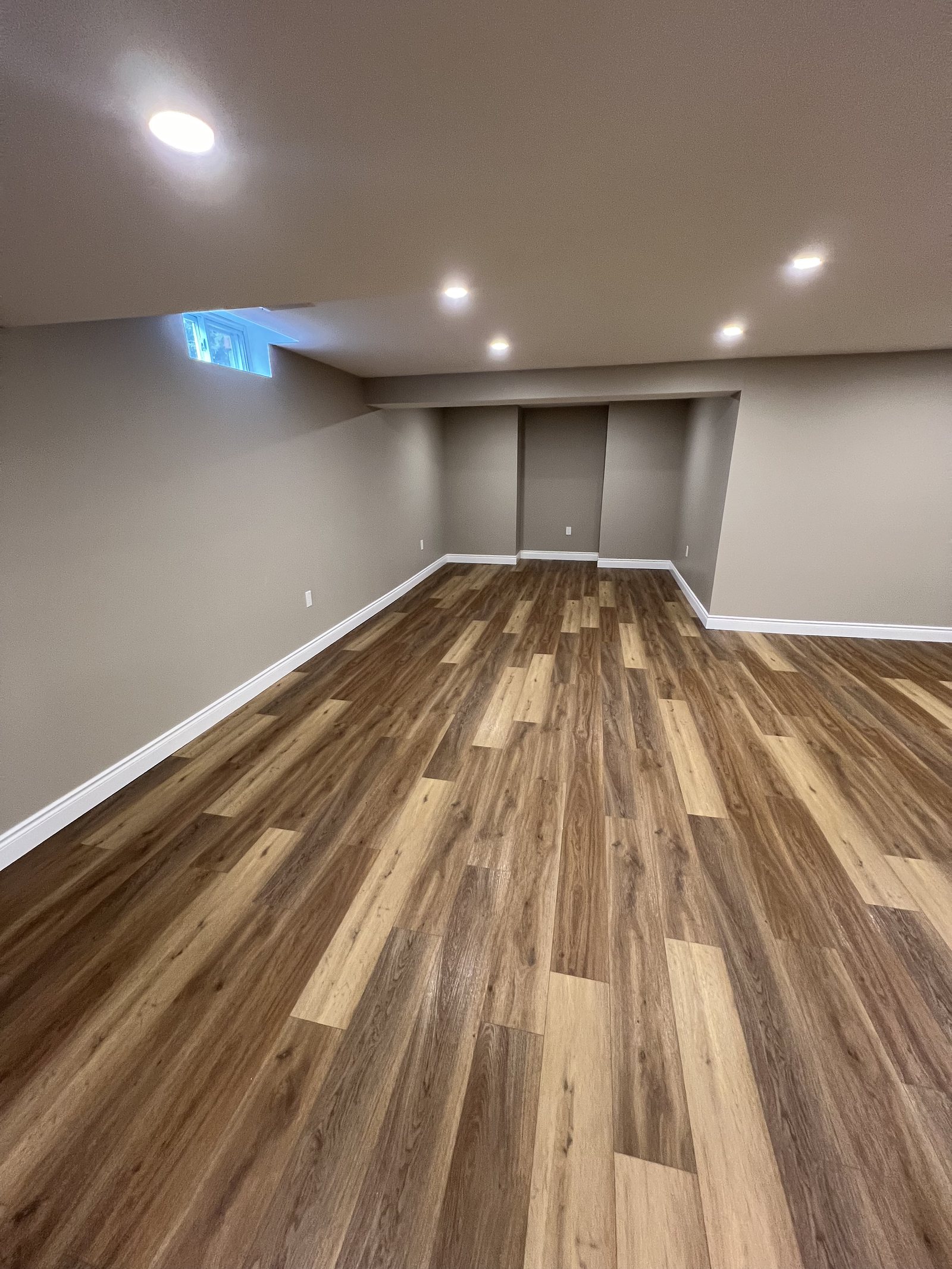 Finished basement with a recessed wall nook, grey walls and wood-look plank flooring