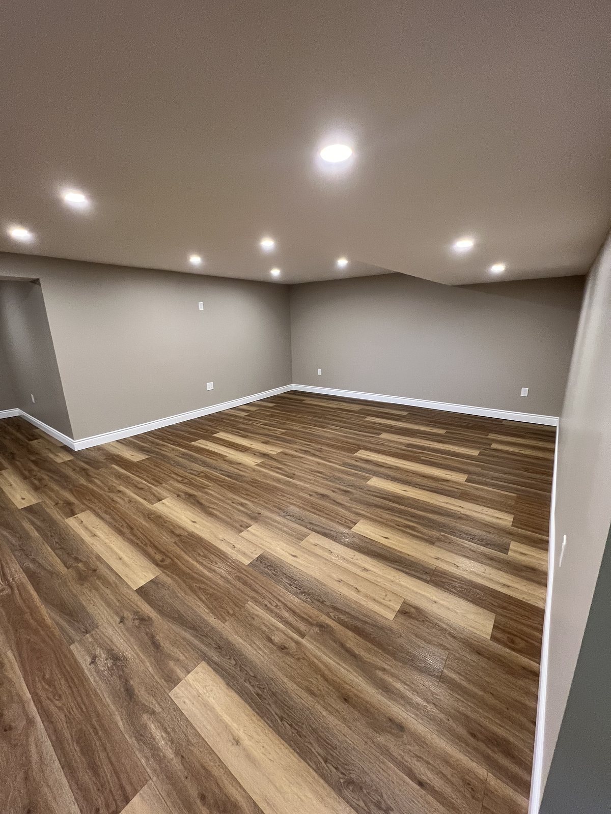 Finished basement with grey walls, recessed pot lights and plank flooring