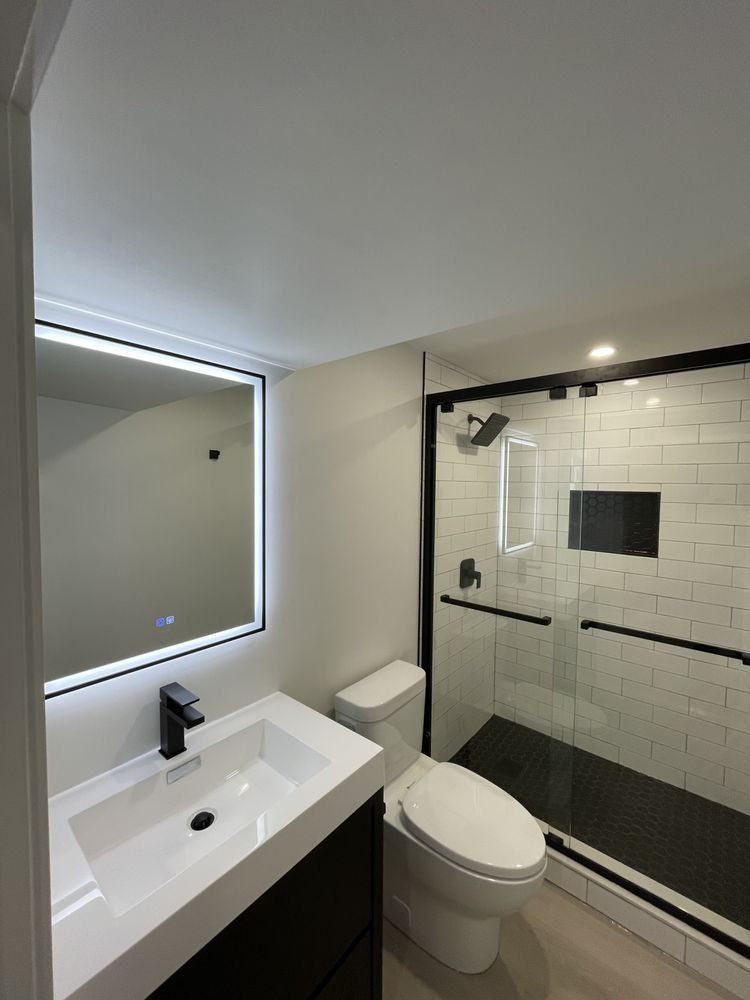 Renovated bathroom with a black floating vanity, backlit LED mirror and a white subway tile glass shower