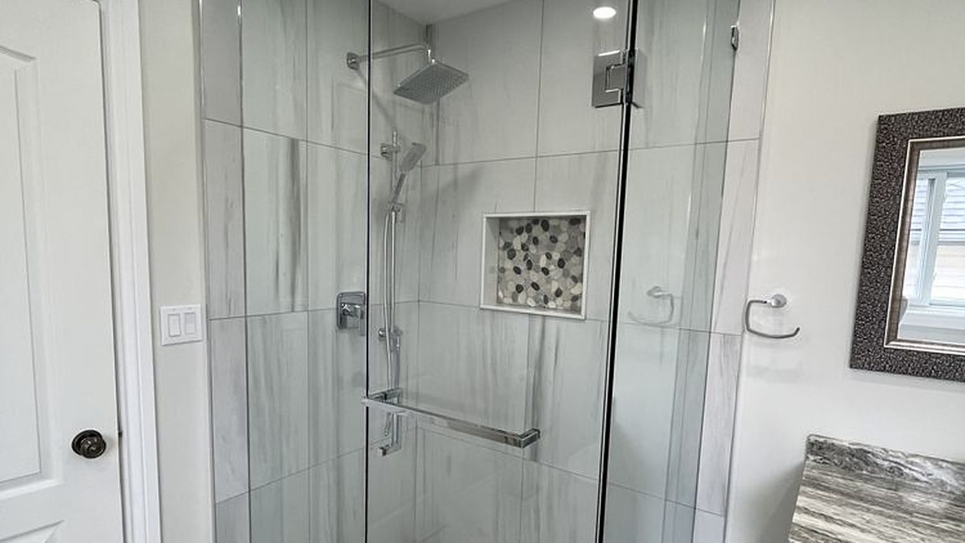 Frameless glass corner shower with vertical marble-look tile and a pebble mosaic shower floor