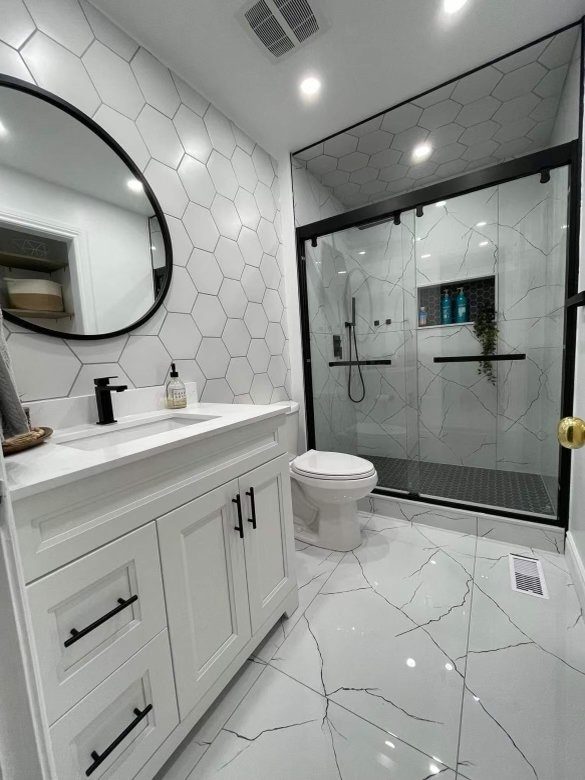 Renovated bathroom with a white hexagon feature wall, round black mirror and marble-look glass shower
