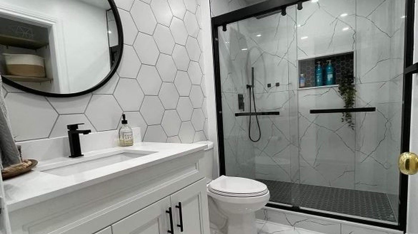 Renovated bathroom with a white hexagon feature wall, round black mirror and marble-look glass shower