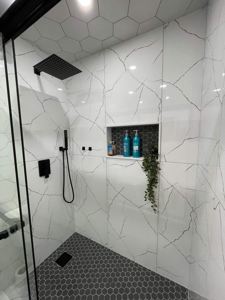 Walk-in shower finished in large-format marble-look porcelain with a black hexagon mosaic floor and matte black fixtures