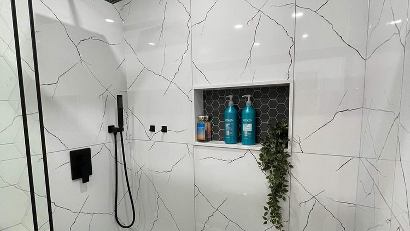 Walk-in shower finished in large-format marble-look porcelain with a black hexagon mosaic floor and matte black fixtures