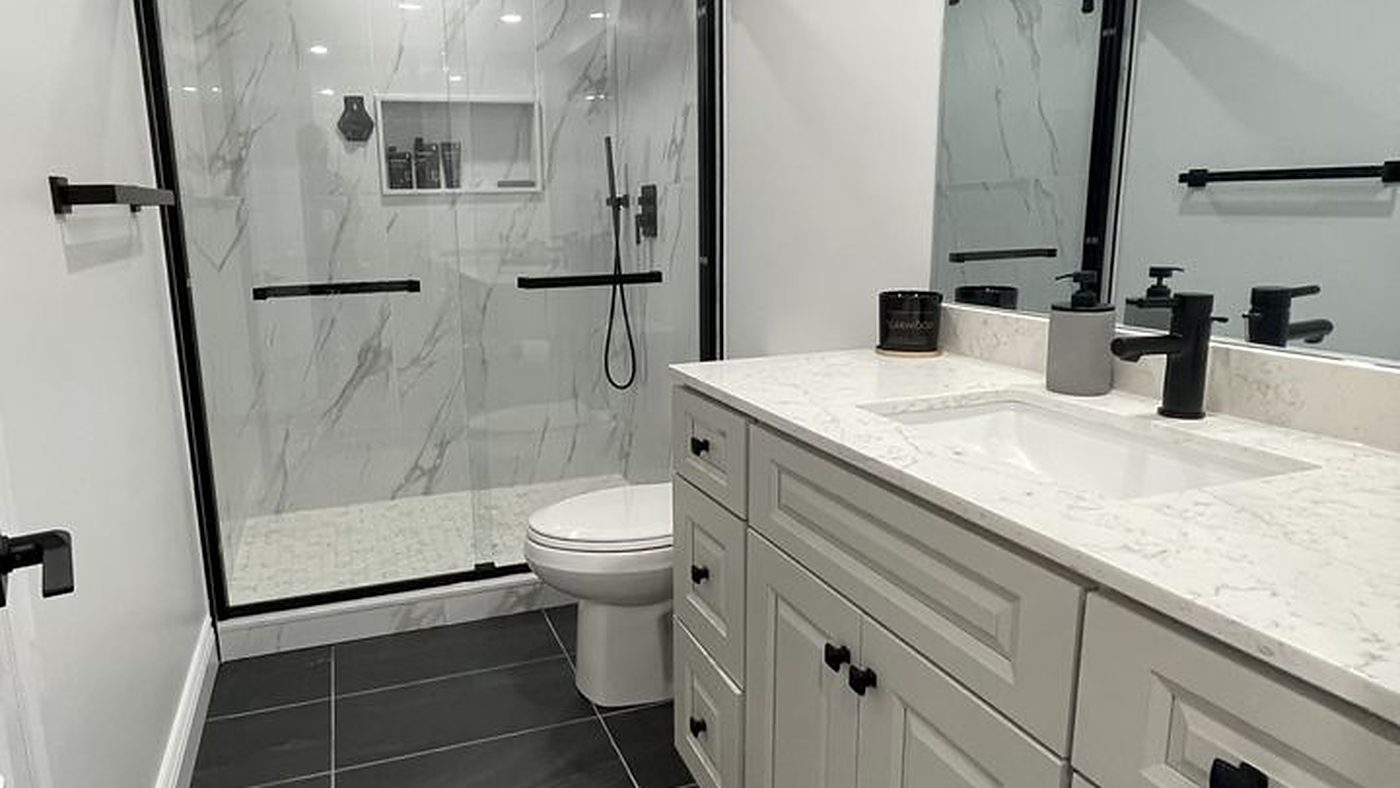 Renovated bathroom with a marble-look glass shower, quartz-topped shaker vanity and dark slate floor tile