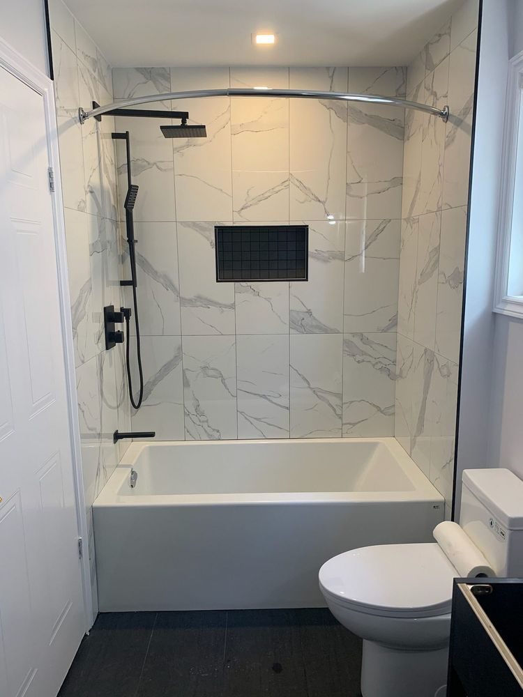 Tub and shower combination finished in marble-look porcelain with matte black fixtures and a tiled niche