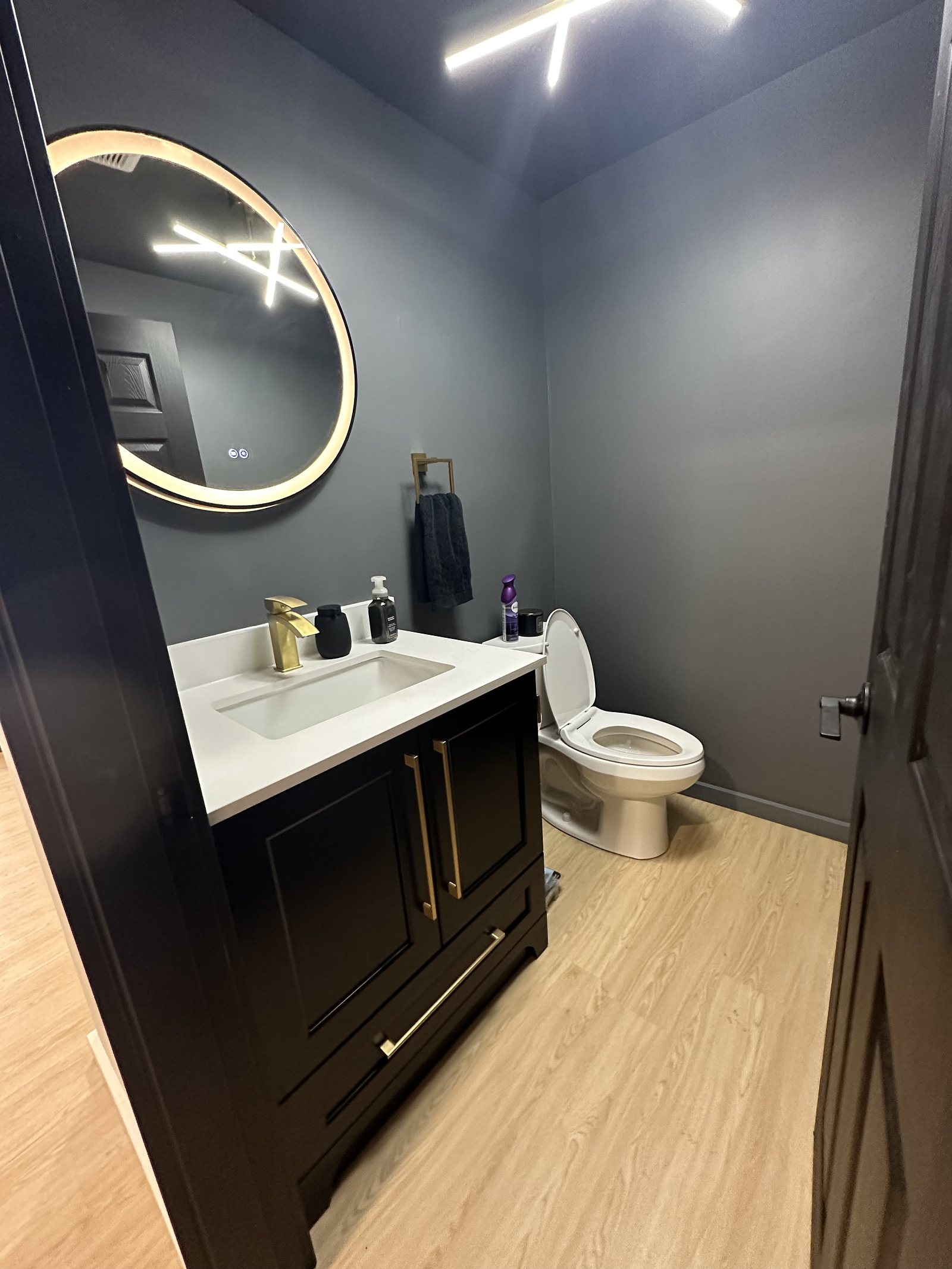 Commercial washroom with a dark vanity, backlit round mirror and gold fixtures