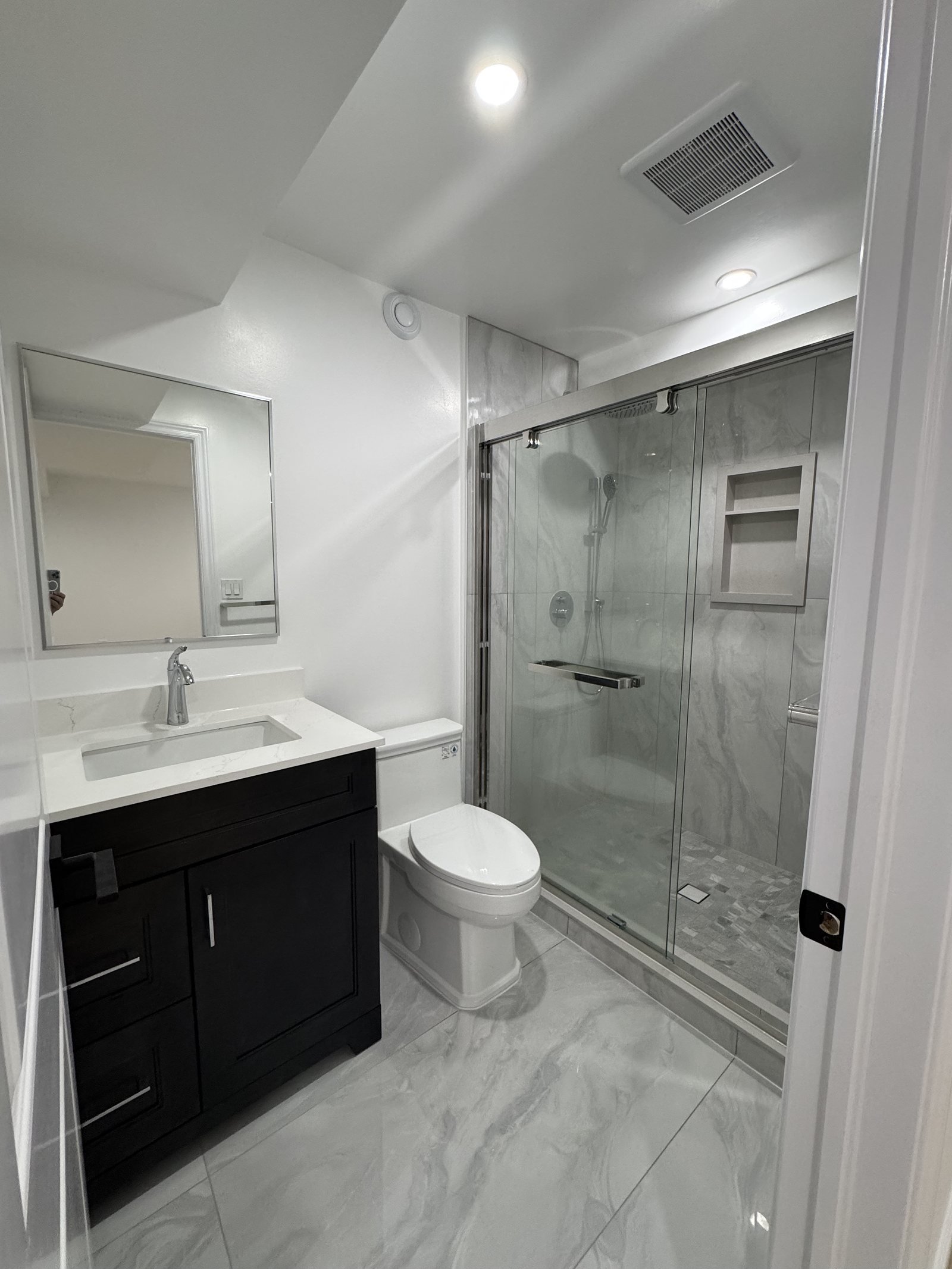 Basement bathroom with a glass shower, dark vanity and marble-look tile