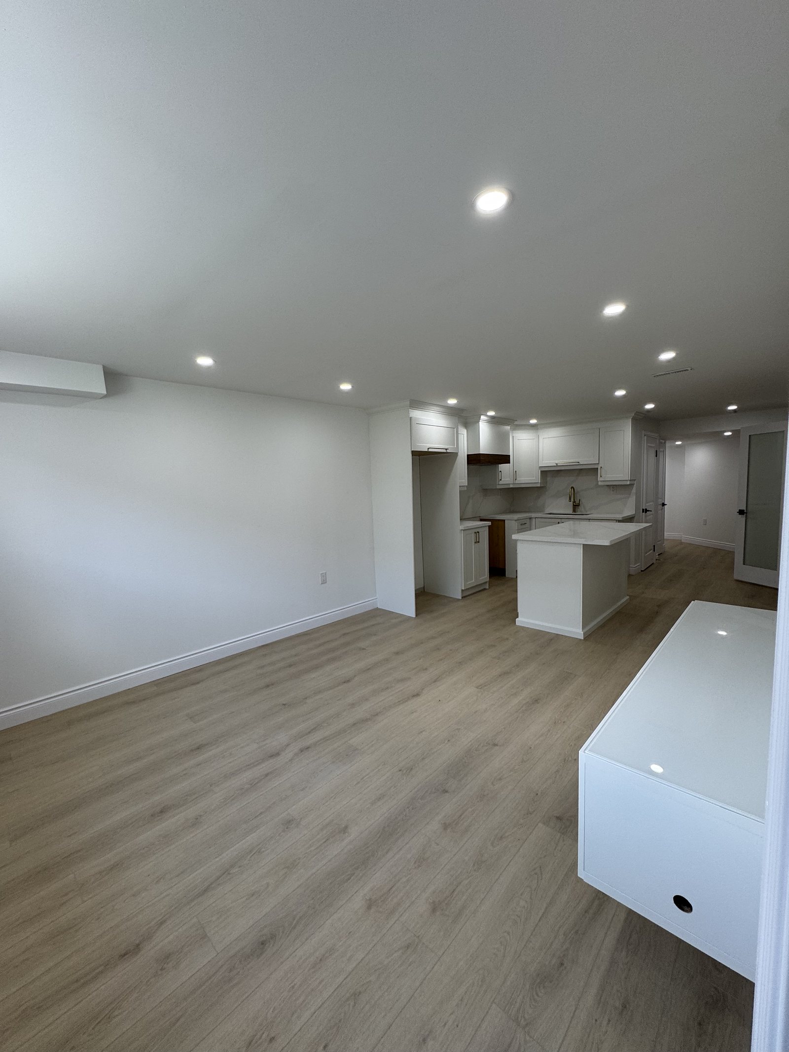 Finished basement living area with plank flooring open to a white kitchen