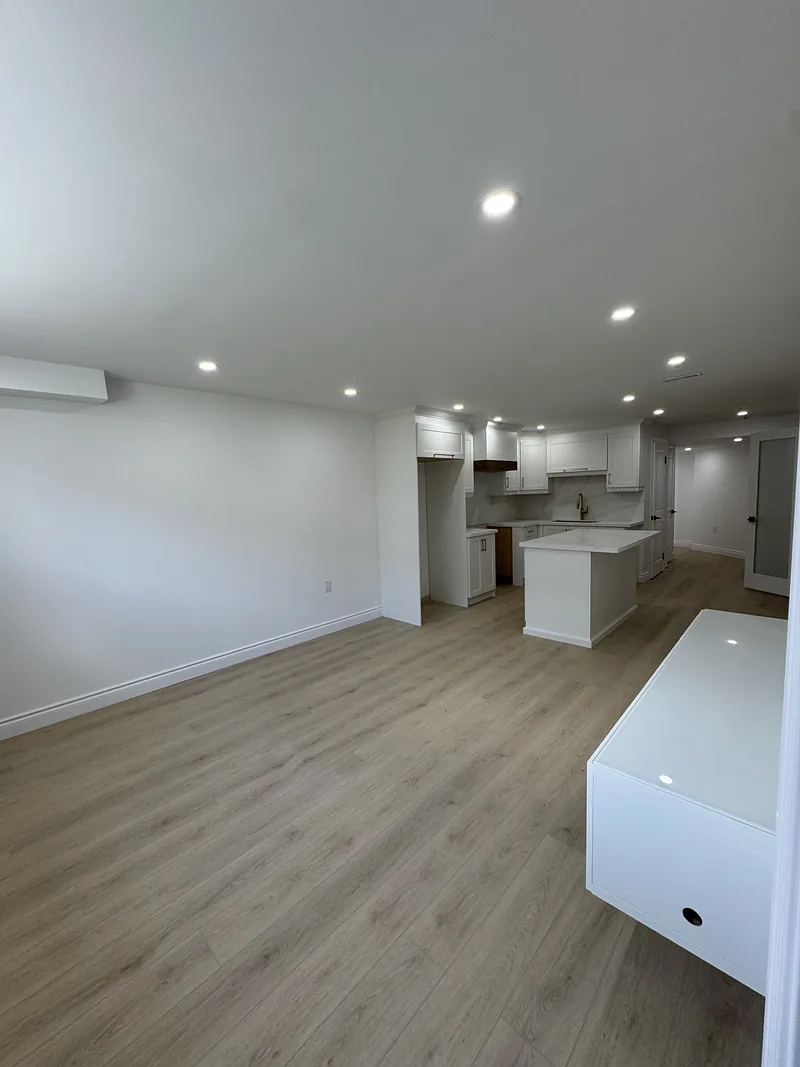 Finished basement living area open to a white kitchen