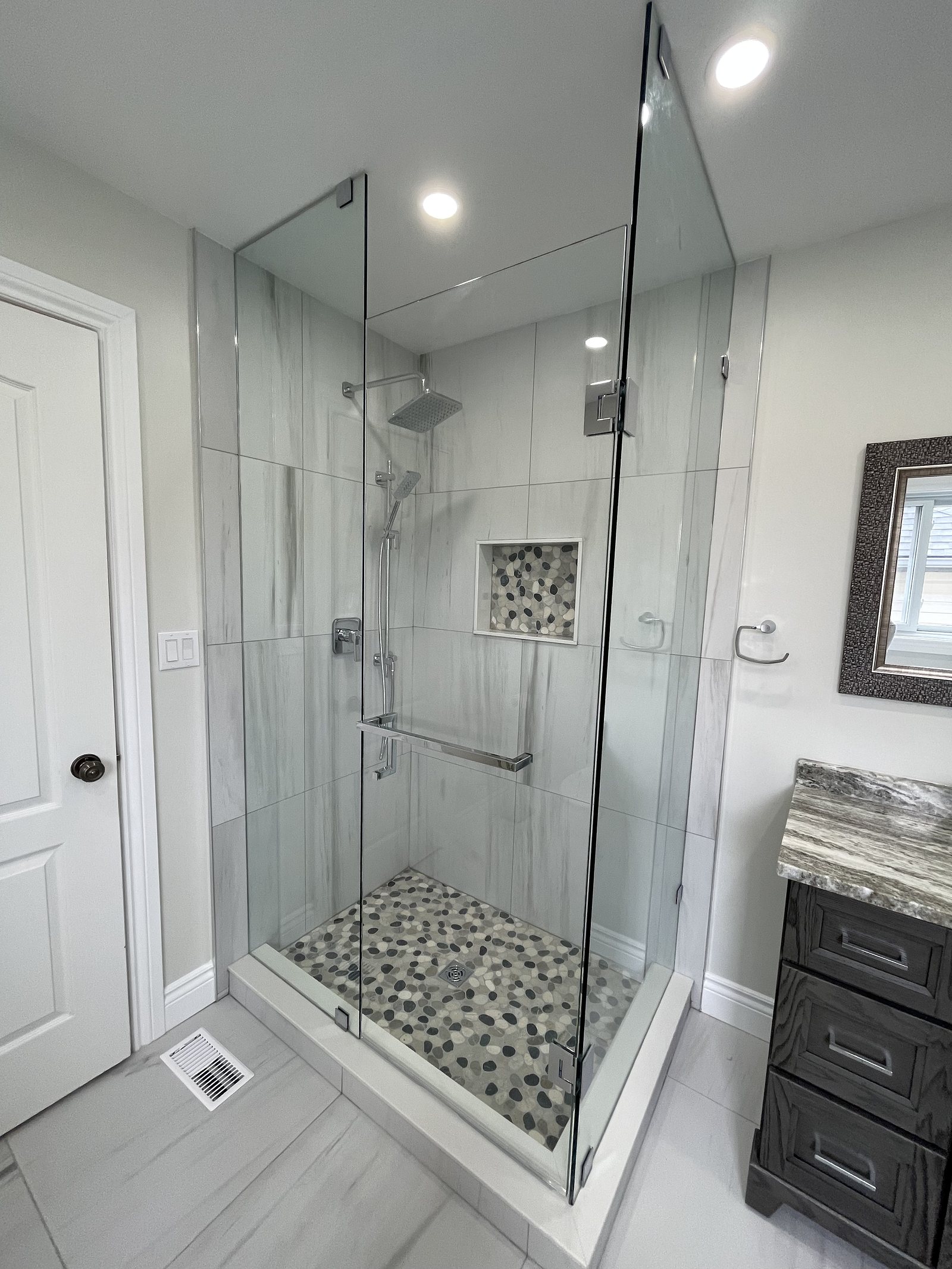 Renovated ensuite with a frameless glass shower, pebble floor and marble-look tile