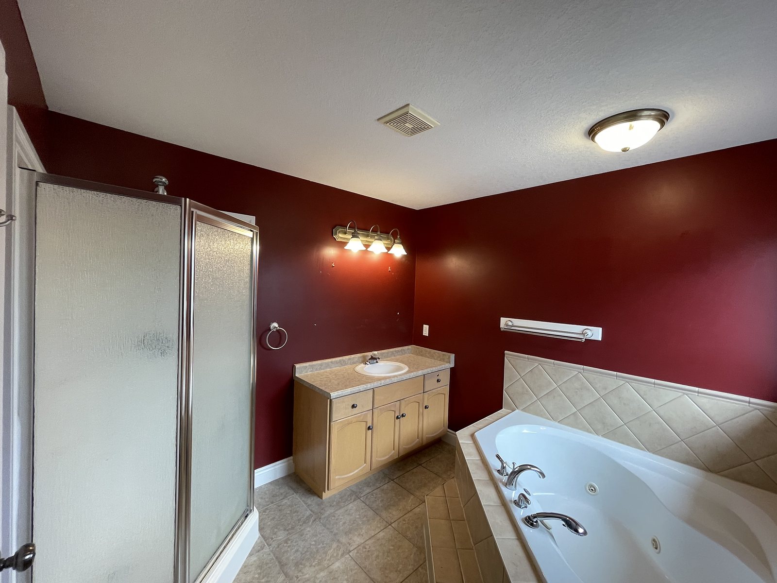 Bathroom before renovation: dark red walls, oak vanity and a corner soaker tub