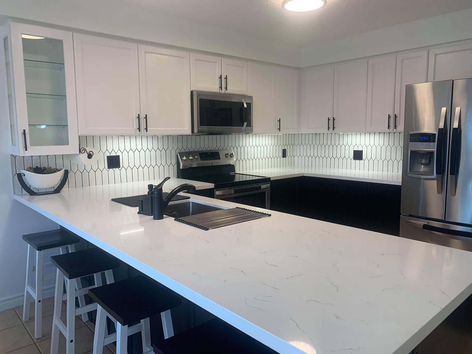 Kitchen with a dark island, white quartz counter and tiled backsplash