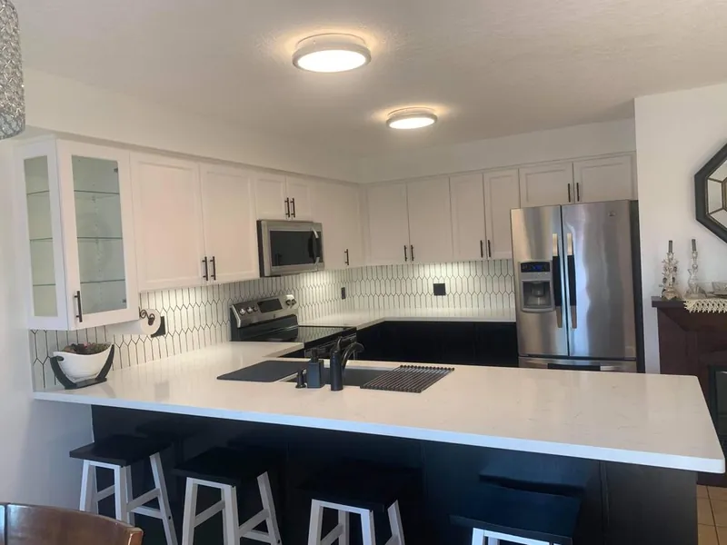 Finished kitchen with white upper cabinets, dark lower cabinetry and a quartz peninsula