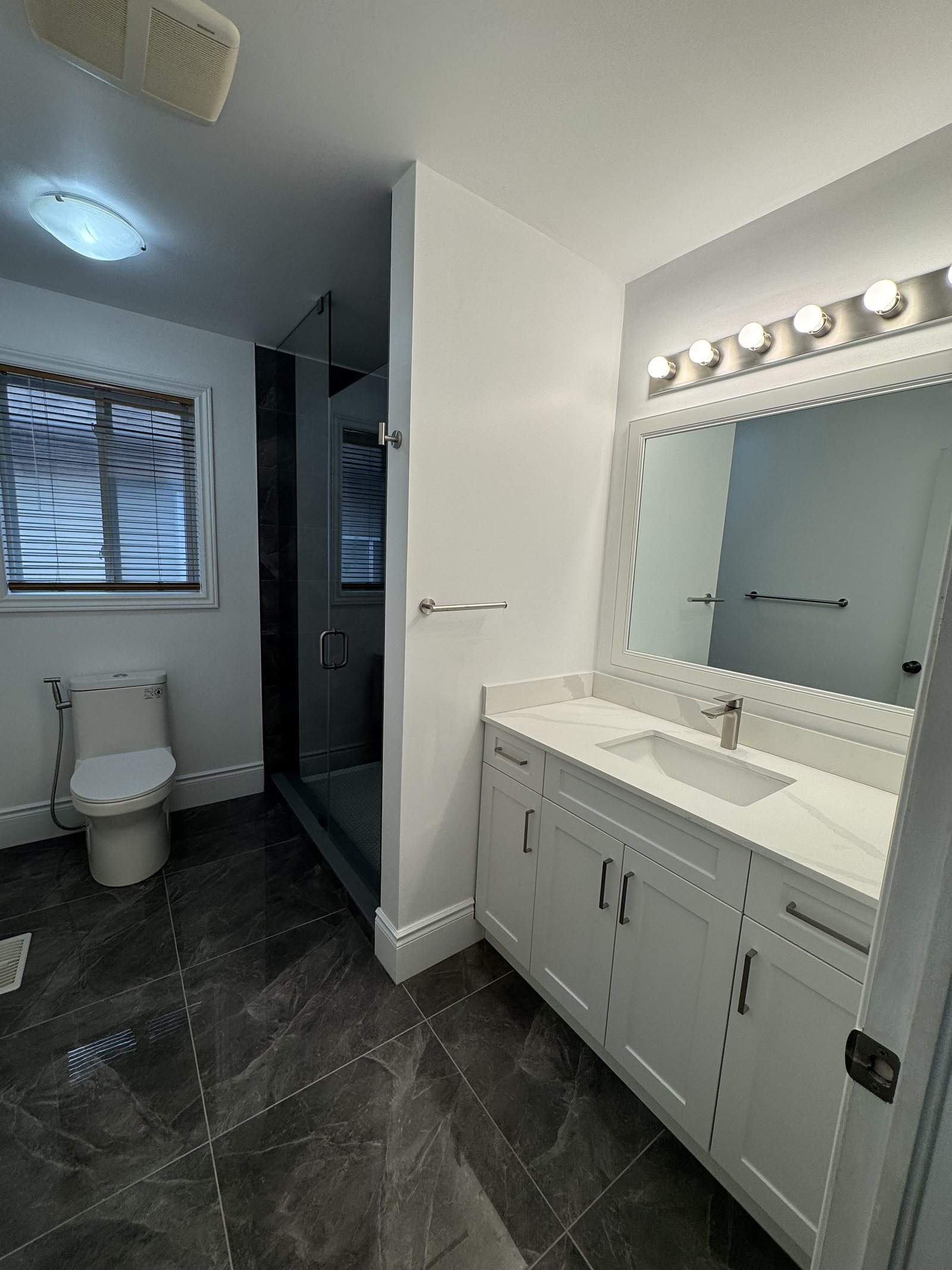 Renovated bathroom with a white shaker vanity, framed mirror and dark marble-look floor tile