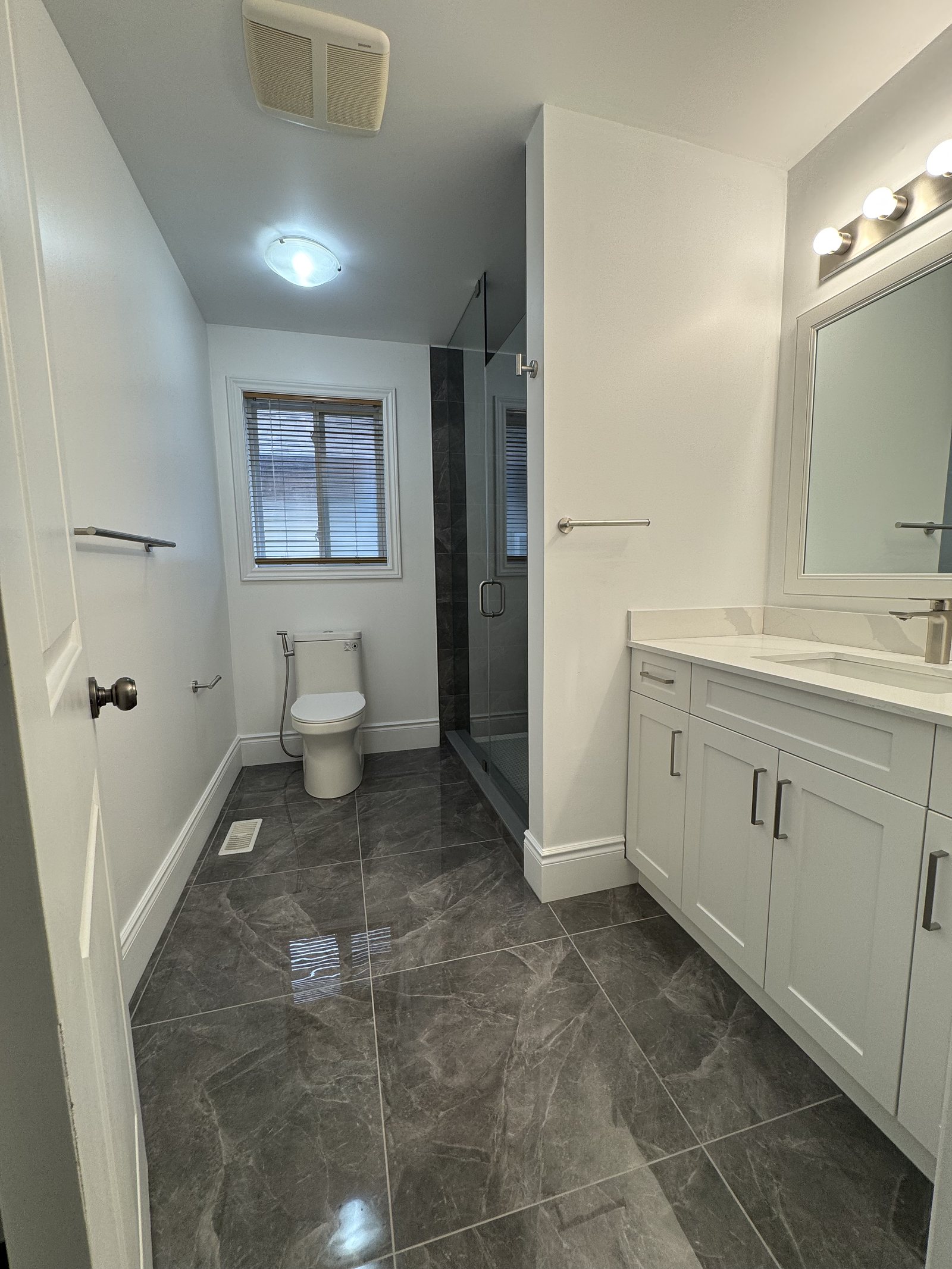 Renovated bathroom with a glass shower, white vanity and large-format floor tile