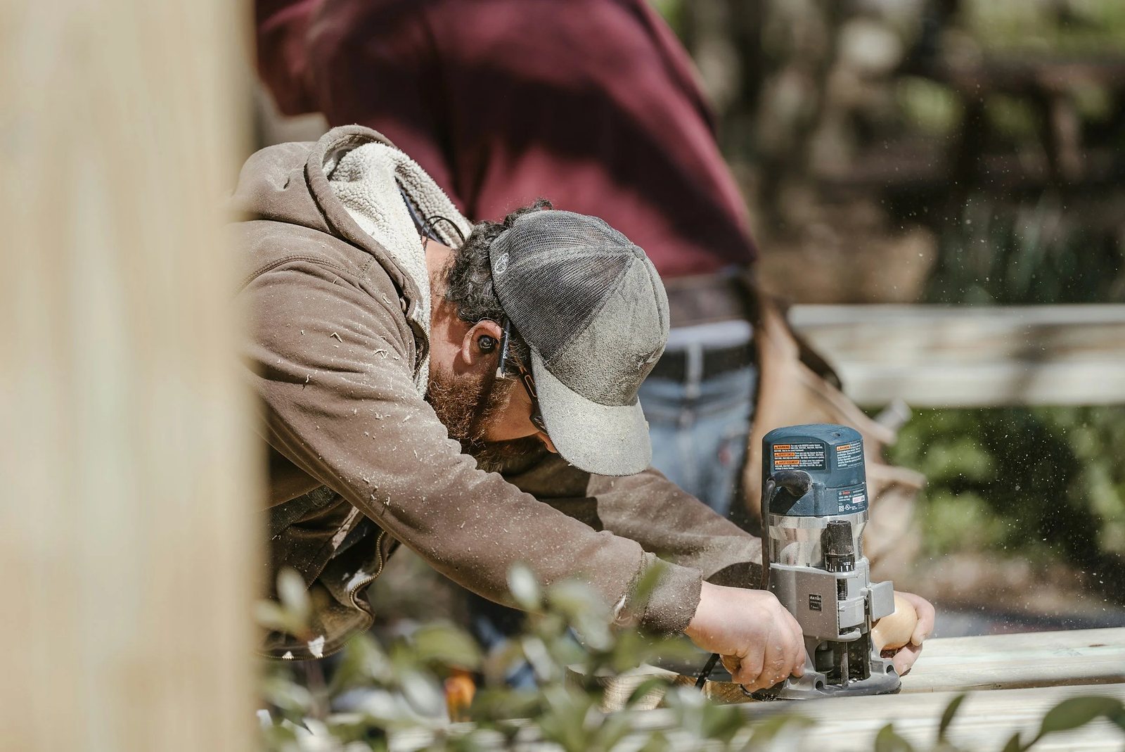 Carpenter guiding a compact router along the edge of a board