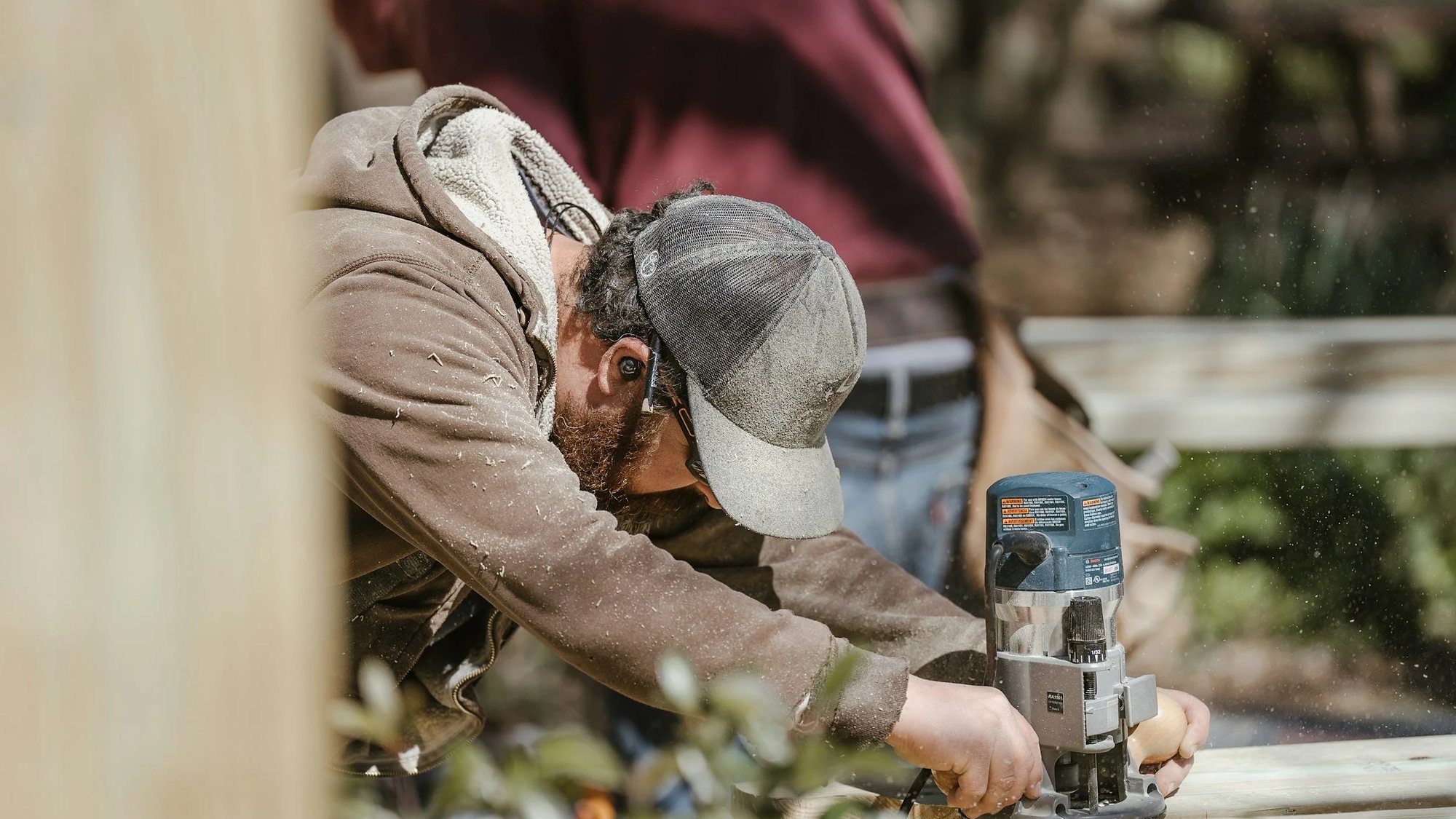 Carpenter guiding a compact router along the edge of a board