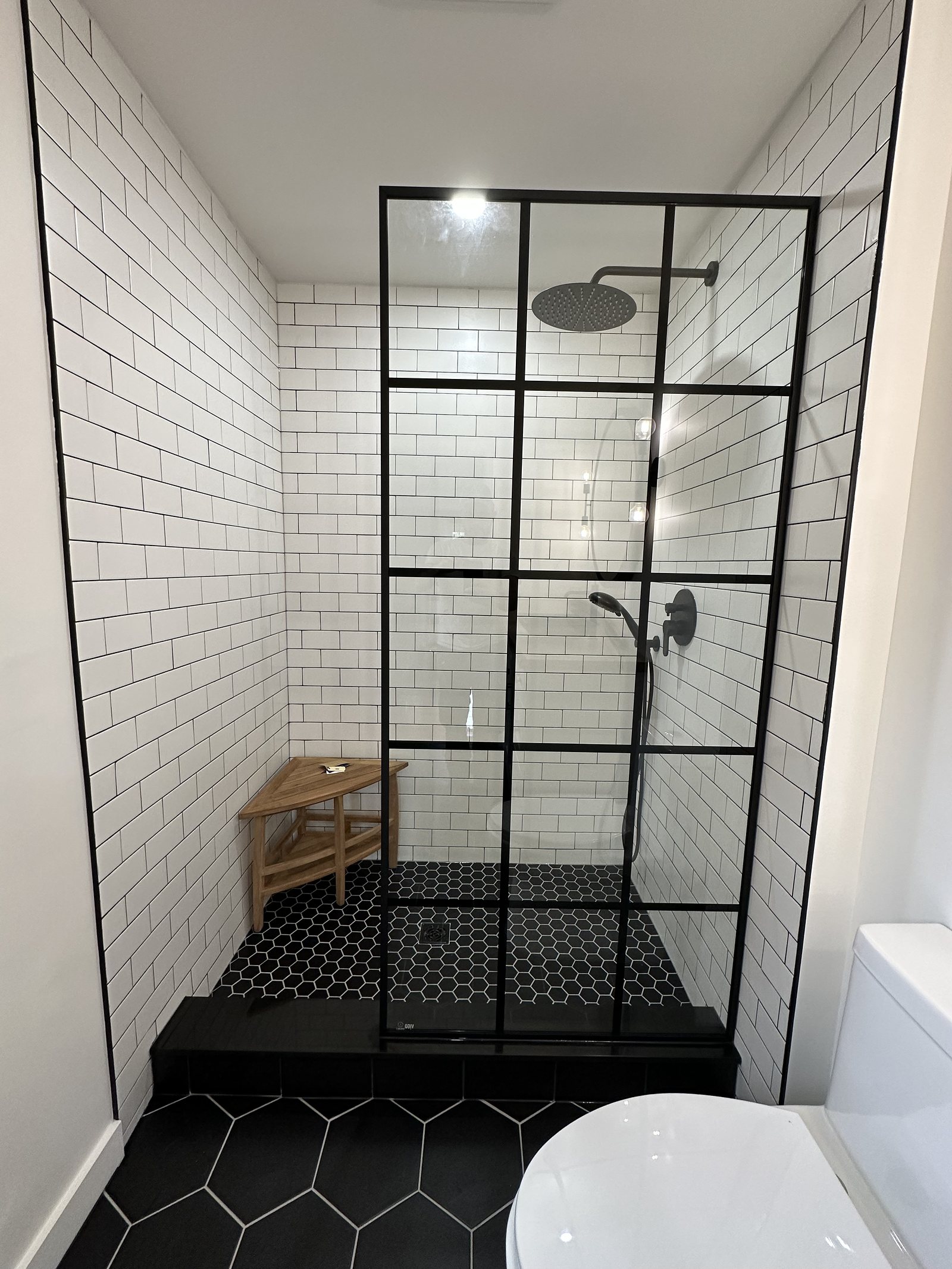 Walk-in shower with white subway tile and a black grid glass screen