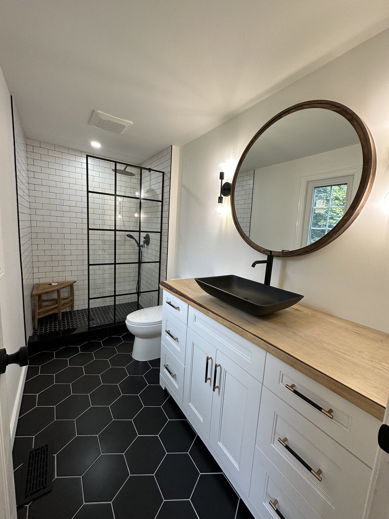 Renovated bathroom with a wood vanity top, black vessel sink and round mirror