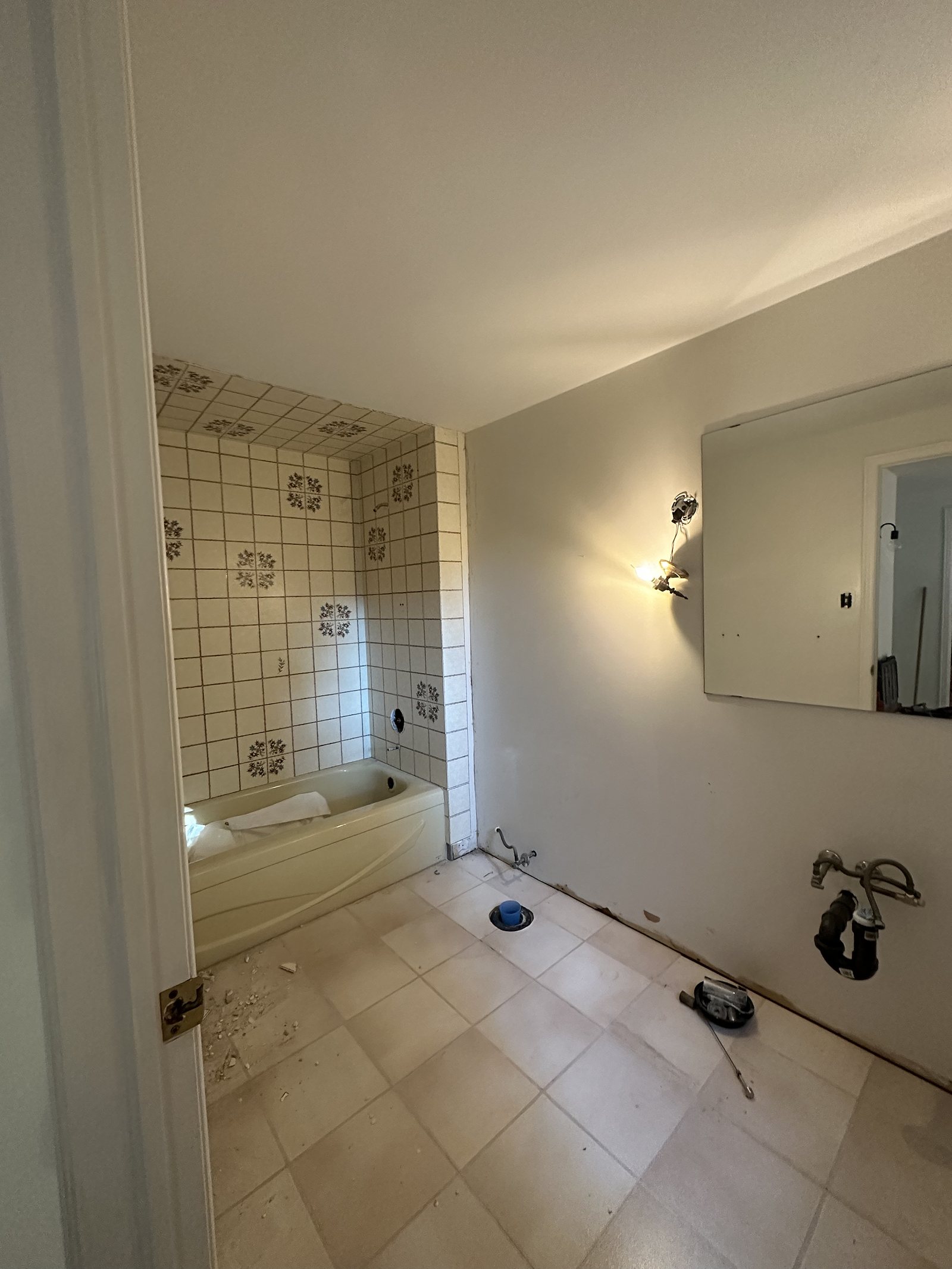 Bathroom before renovation: dated tub surround and beige floor tile